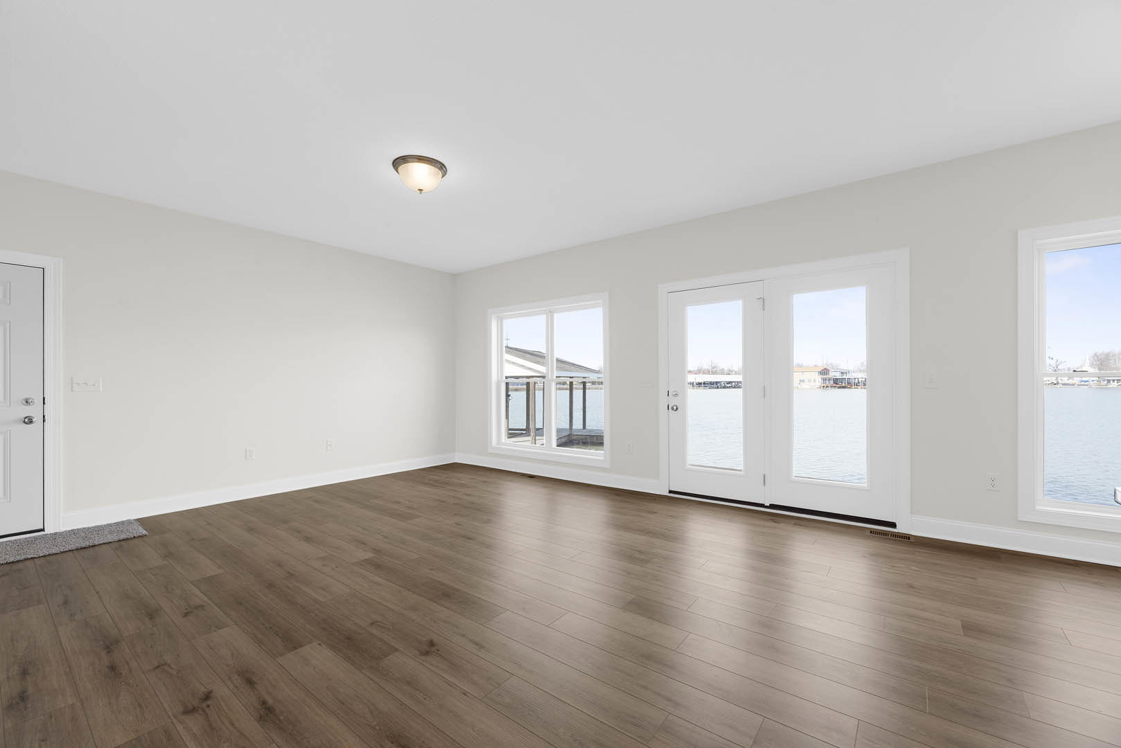 Hardwood floor in a spacious room with plaster walls, double doors opening to a water view, large windows, and ceiling light fixture