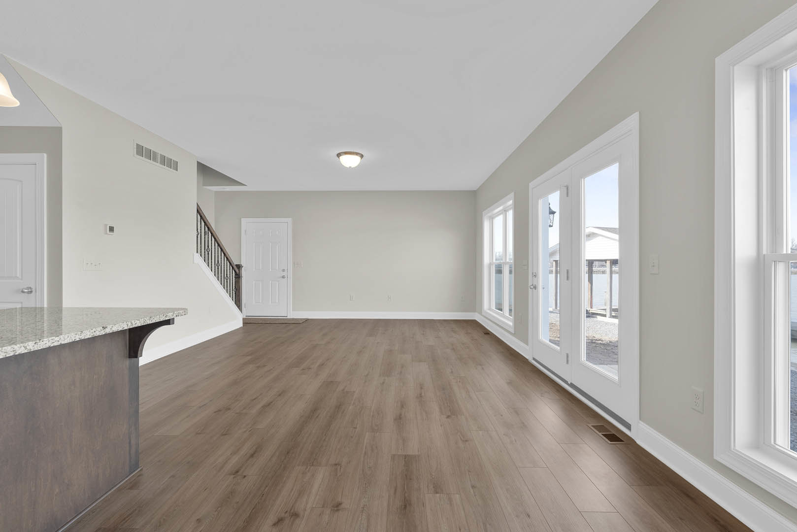 Wood flooring in a room with a marble table, white door with silver knobs, ceiling light fixture, and window.