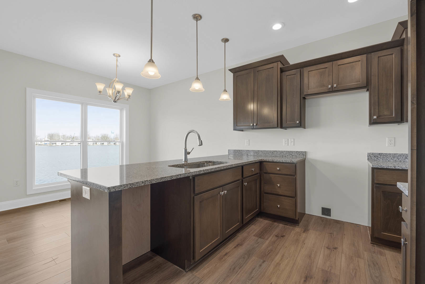 Marble countertop kitchen with undermount sink, chrome faucet, white cabinetry, and large window overlooking water