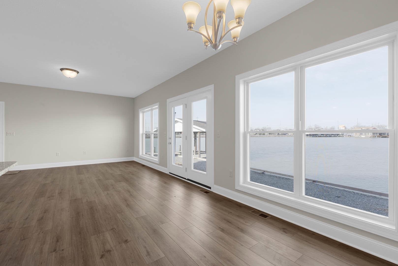 Hardwood floor living area with large windows overlooking water, ornate chandelier hanging from ceiling, white walls with crown molding