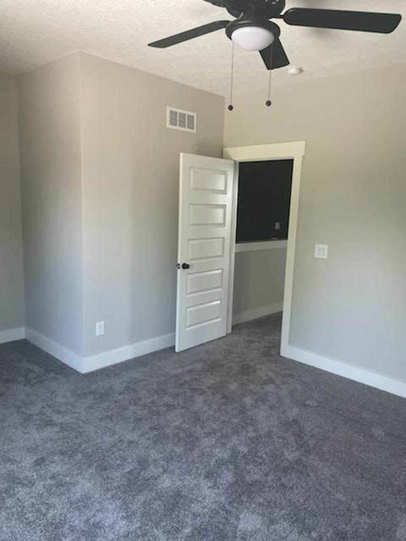 Carpeted bedroom with white trim, open white door featuring black knobs, ceiling fan with light, window with vent, neutral walls