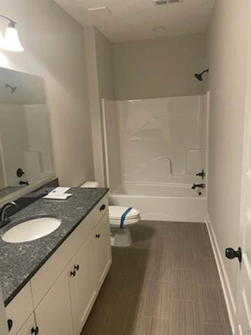 Modern bathroom with white porcelain sink, chrome faucet, wall-mounted mirror, and toilet; light gray tile flooring and neutral wall tiles.
