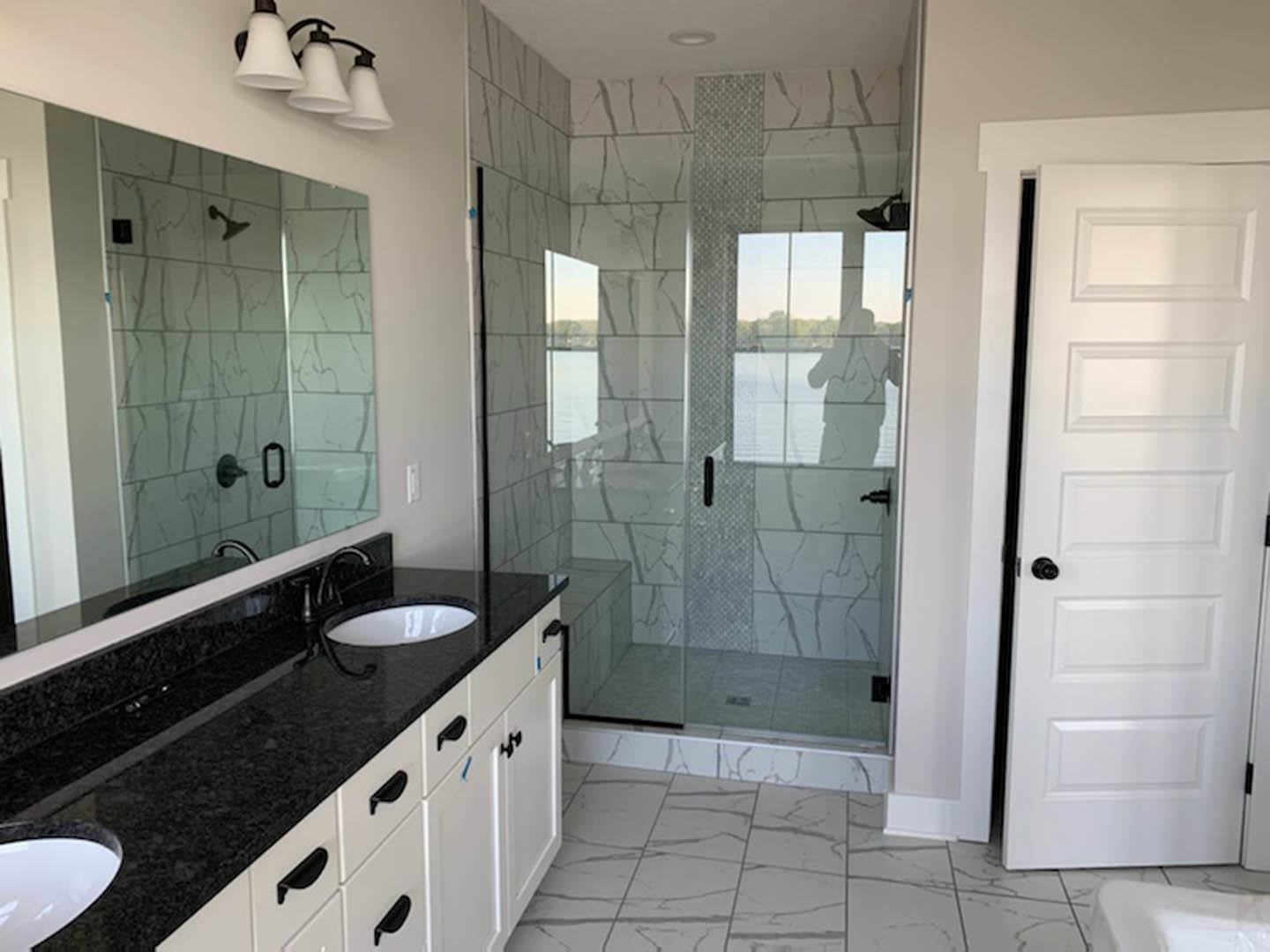 Modern bathroom featuring a frameless glass shower enclosure, white vessel sink on a quartz countertop, matte black faucet and hardware, white paneled door with black knob