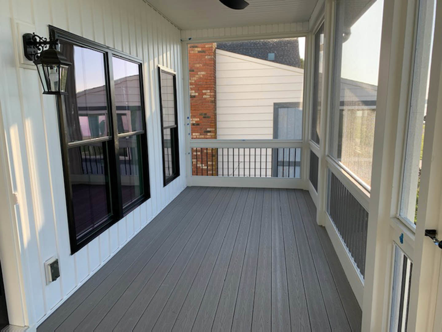 Covered porch with black ceiling fan, black-framed windows, wood deck flooring, and metal railing