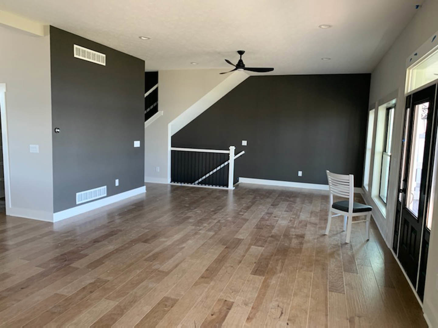 Hardwood floor room with white chair featuring black cushion, white ceiling with black ceiling fan, black gate with white bars, neutral walls