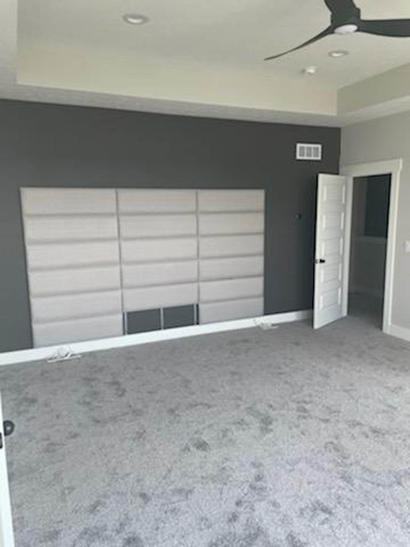 White paneled wall, grey carpet flooring, ceiling fan, window, white door with glass inset and black handle
