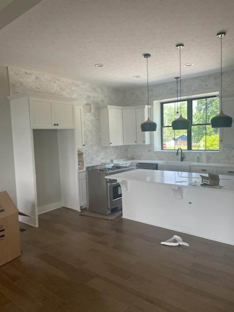 White kitchen cabinets, stainless steel stove and oven, wood flooring, white wall with black stripes, cluster of pendant lights, white triangular dish with brown food on