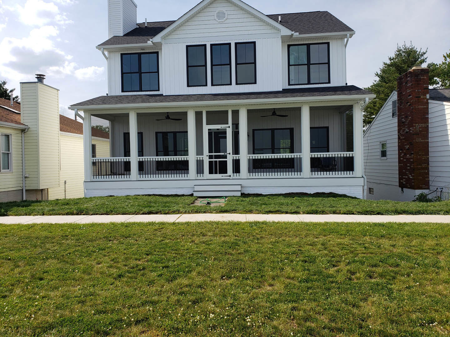 Large white house with brick and white siding, covered front porch, manicured lawn, sidewalk, prominent windows, and gutter system under a clear sky.