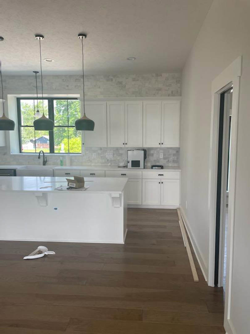 White kitchen cabinets with brushed metal handles, wood plank flooring, white quartz countertop, stainless steel sink, and a white door with a square window.