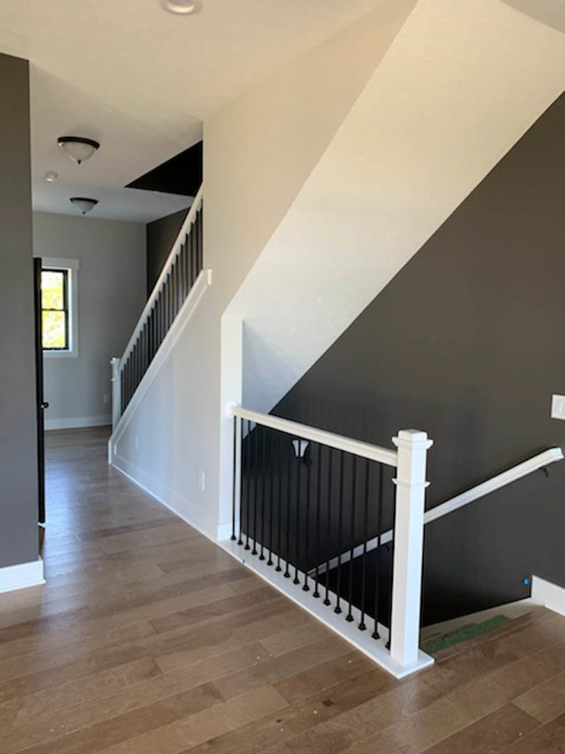 Wood staircase with white balusters and black handrail, hardwood flooring, large window with yellow wall, close-up of modern lamp.