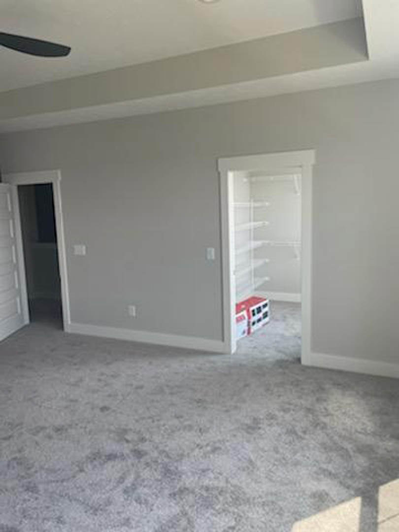 Carpeted room featuring built-in shelves, open white door with glass window, white walls, black frame accents, and ceiling plaster.