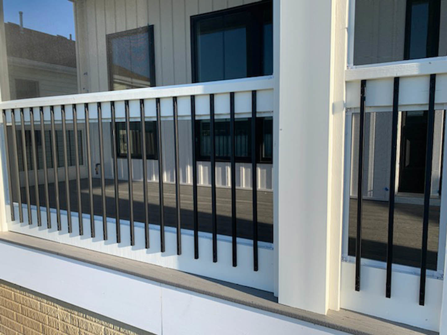 White deck with black metal railing, glass door partially open, close-up of window and baluster details on residential exterior.