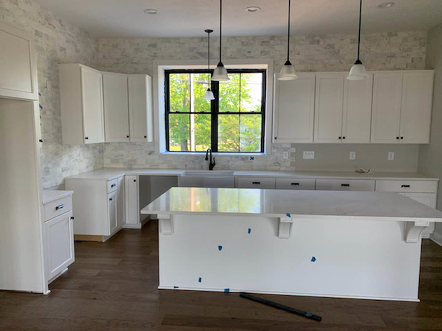 White kitchen with shaker cabinets, stainless sink under a window, light tile backsplash, quartz countertops, and wood flooring.