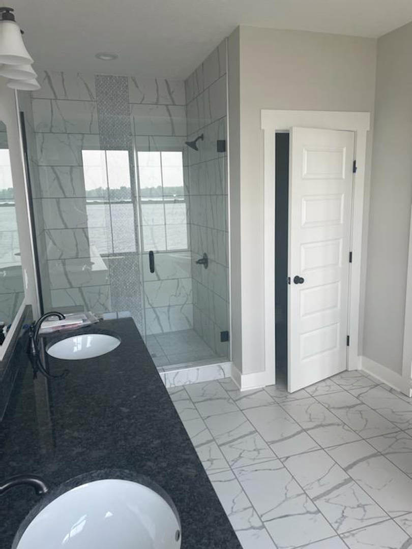 Bathroom featuring a frameless glass shower enclosure, white ceramic sink with chrome faucet, large wall mirror, and white tile flooring with black accents
