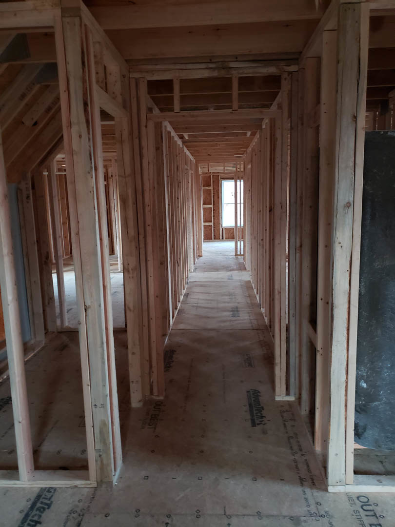 Unfinished hallway with exposed wooden beams, plaster walls, construction materials, and a window letting in natural light