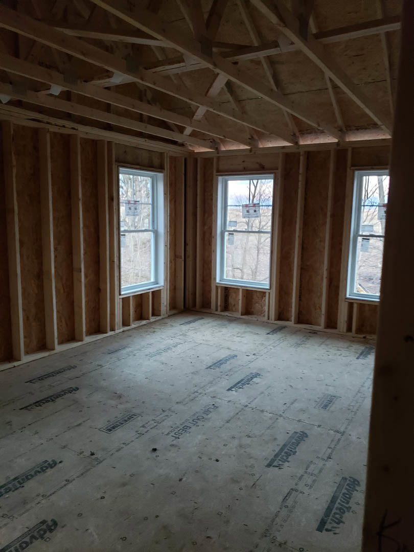 Spacious room featuring exposed wood ceiling beams, large windows with daylight streaming in, and neutral walls