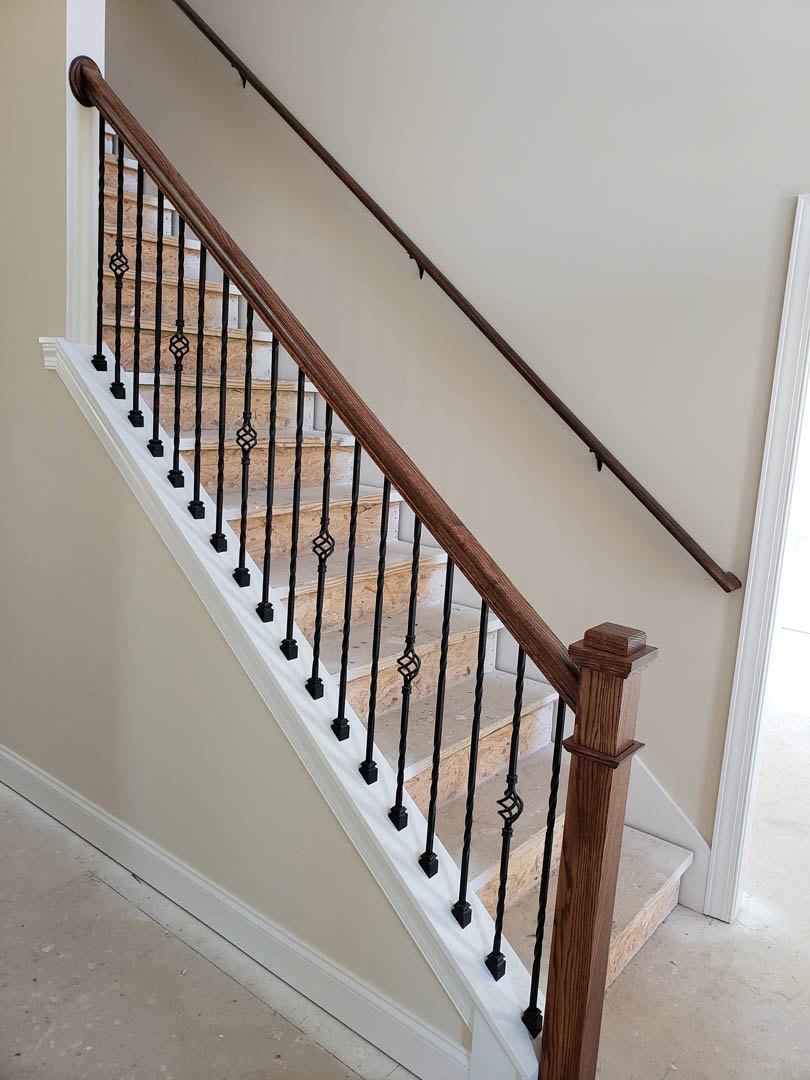 Modern staircase with black metal railings, wooden post, and close-up view of handrail against a neutral wall