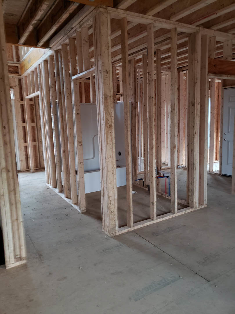Unfinished bathroom with exposed wood framing, white door with silver handle, and white toilet on subfloor