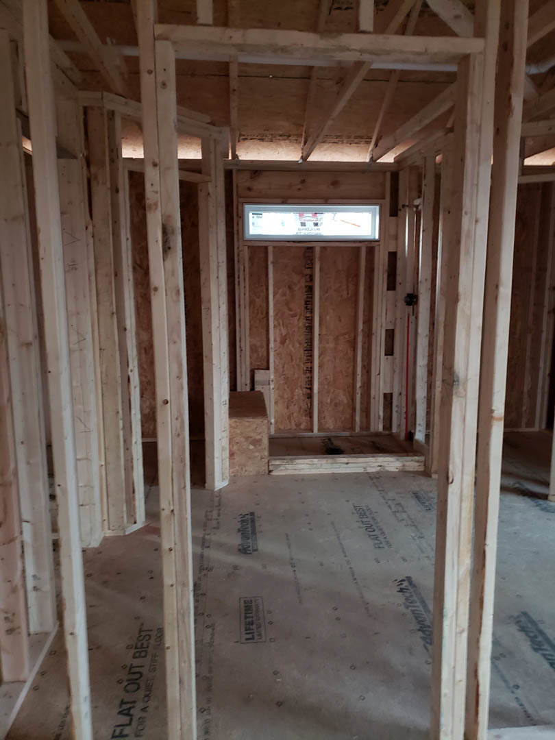 Room under construction with exposed wood framing, ceiling beams, unfinished walls, and subfloor marked with black text