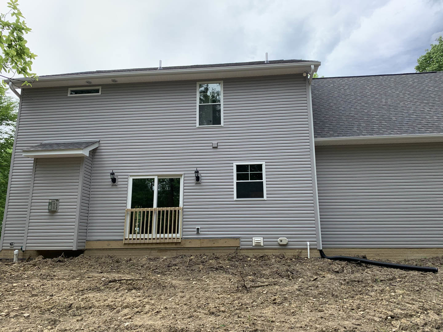 Two-story home with light siding, white-framed windows, wooden balcony railing, and bare dirt yard under a partly cloudy sky