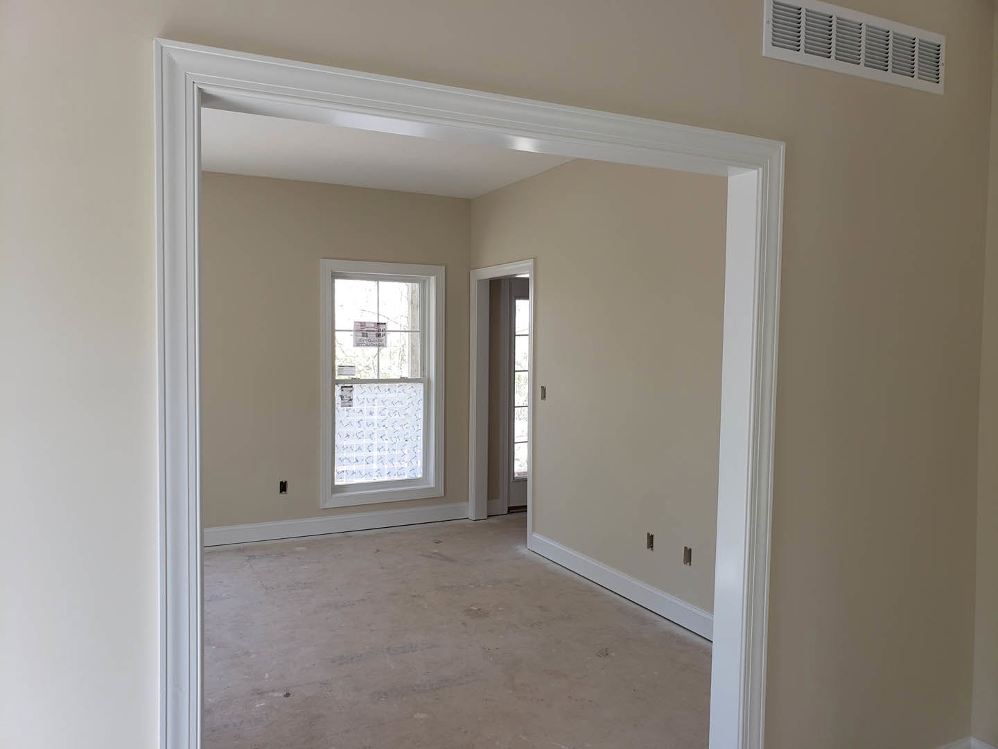 Hallway with plaster walls, white door frame, wood flooring, wall vent, and window displaying a sign
