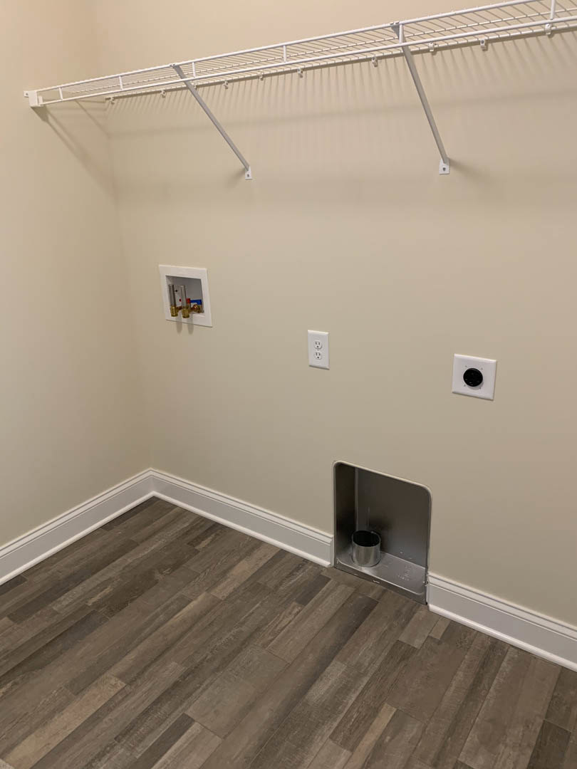 Clothes rack against white plaster wall, laminate flooring, metal trash can in corner, wall-mounted water heater, ceiling fixture visible