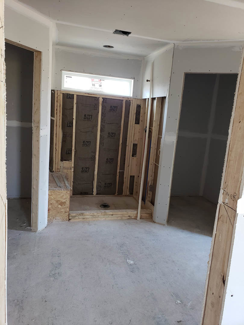 Walk-in shower with glass enclosure, large window, plaster walls, recessed ceiling light, concrete and wood flooring transition