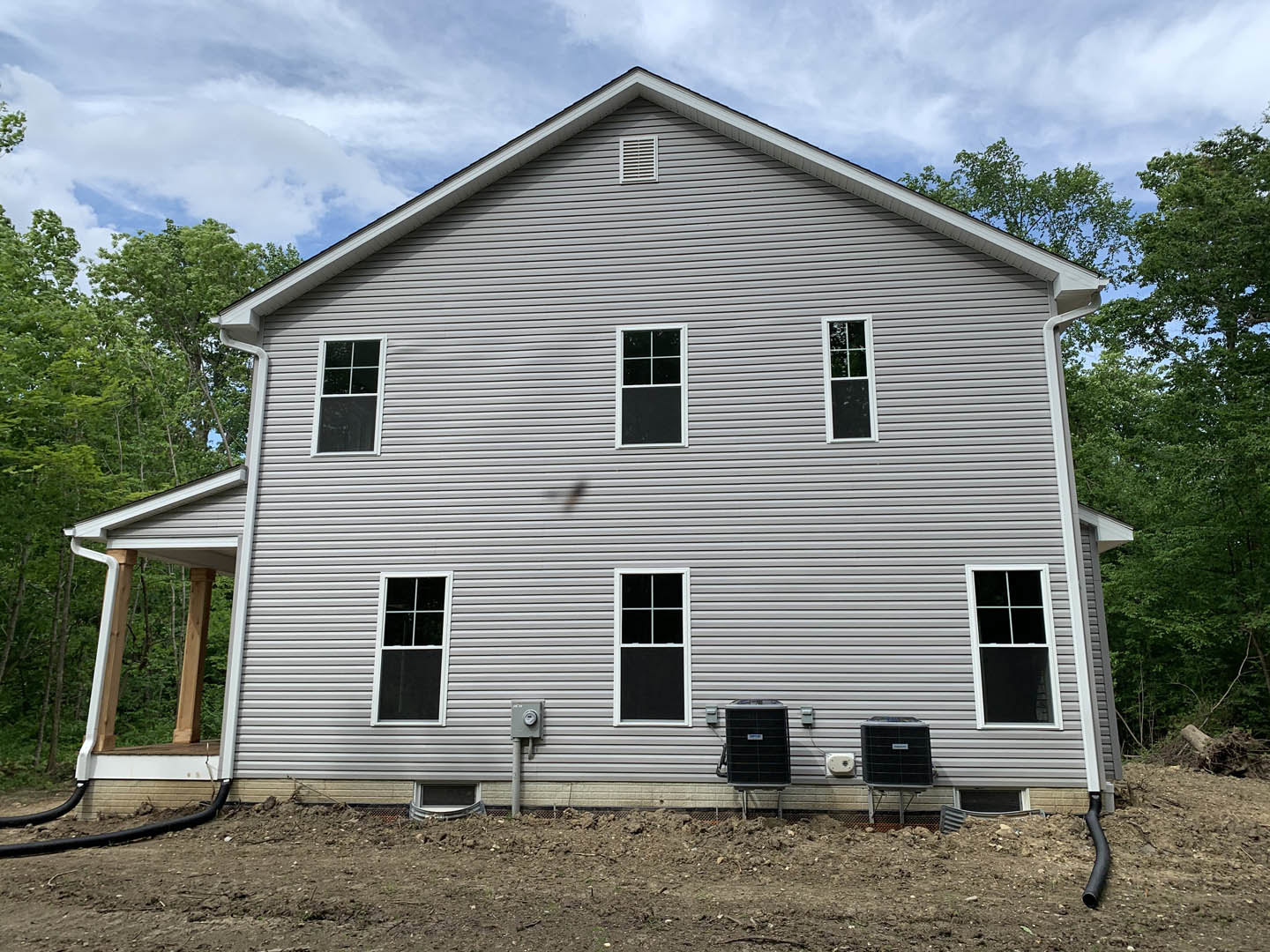 Grey-sided house with minimal windows, white-framed and black-paneled window, white vent, black rectangular object with metal grate, Rockingham Meeting House visible in background