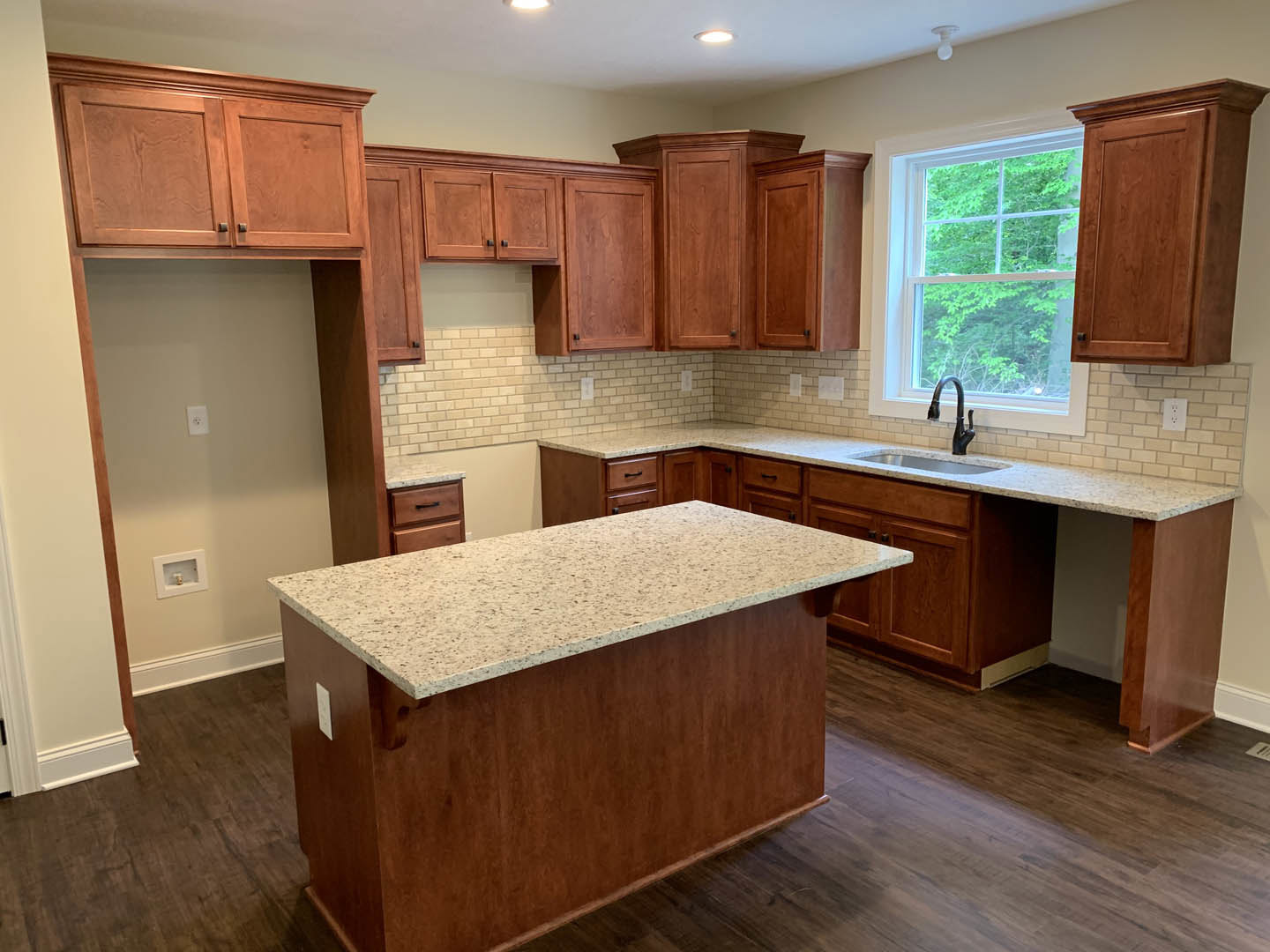 Granite countertop with undermount sink and curved black faucet, white cabinetry, large window overlooking trees, light wood flooring