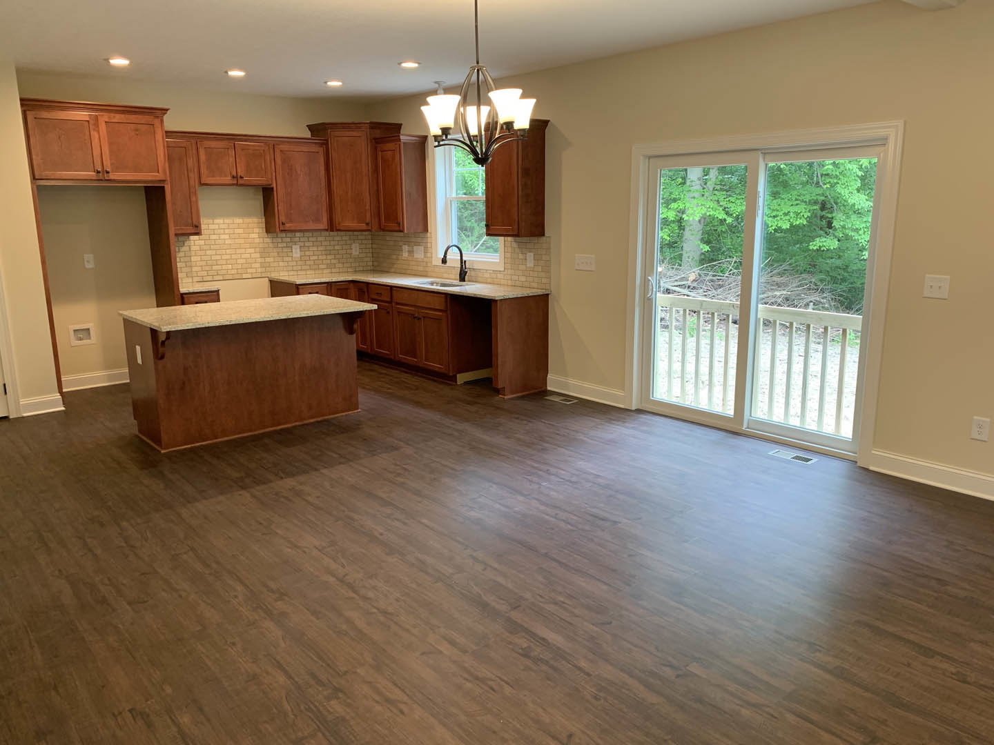 Kitchen with hardwood flooring, large sliding glass door opening to deck and trees, modern cabinetry, stone countertop, and multi-bulb ceiling light fixture