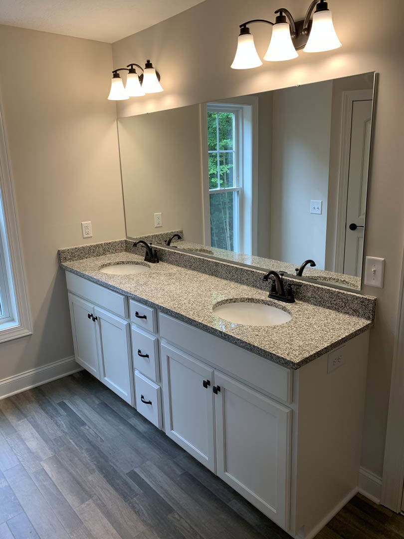 White bathroom with double vanity, quartz countertop, two undermount sinks, large frameless mirror, brushed nickel faucets, three-light fixture above, shaker-style cabinetry, light