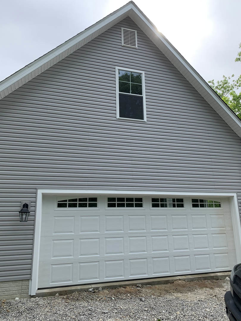 Modern house exterior with light-colored siding, white-framed window, single garage door, gravel landscaping, and partial view of a parked car