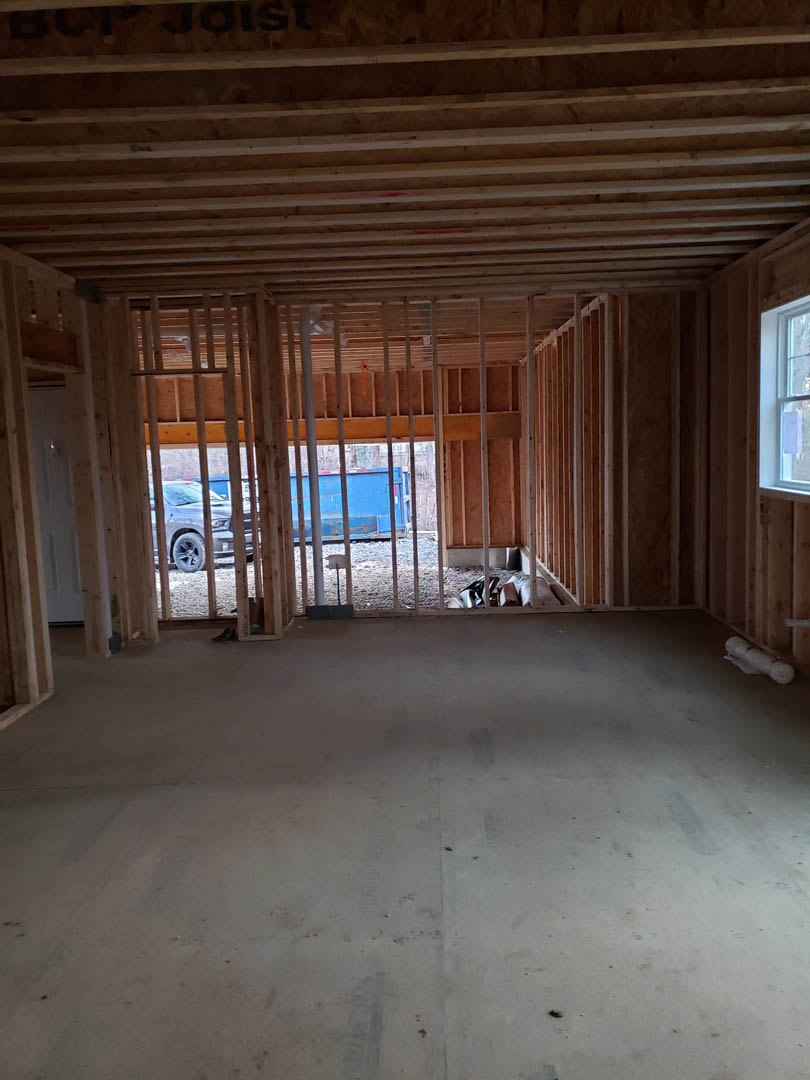 Room with light wood flooring, exposed wooden ceiling beams, large window with white frame, and parked car visible outside.