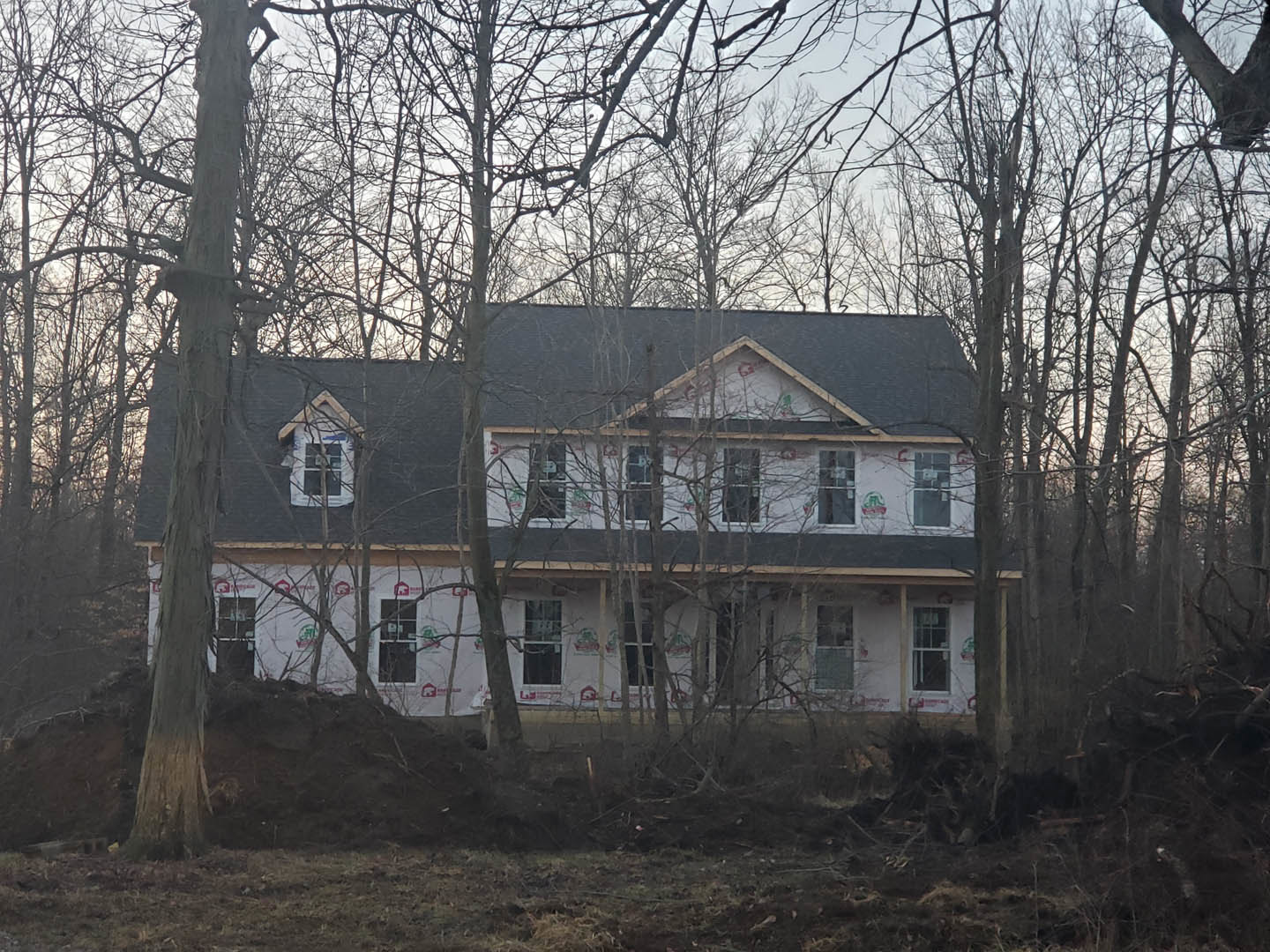 Two-story house with white-framed windows, surrounded by leafless trees and tree trunks, winter landscape