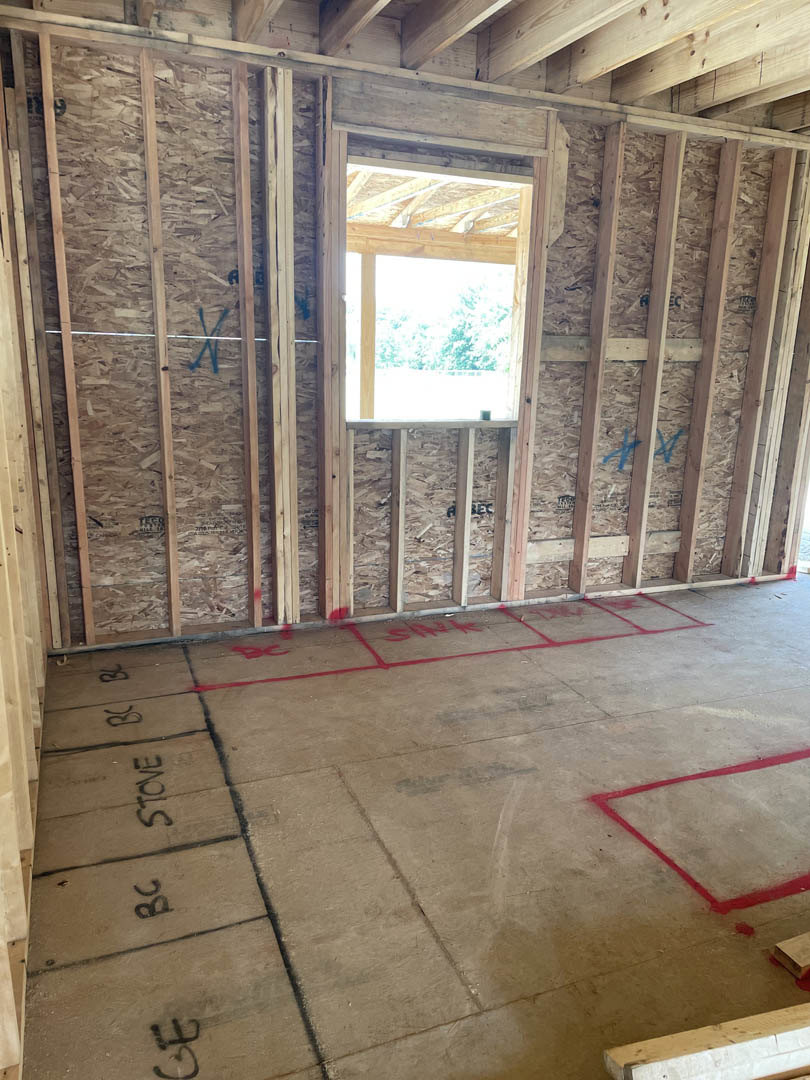 Concrete floor with red painted markings, unfinished walls with exposed wooden framing, window letting in natural light, ceiling insulation visible.