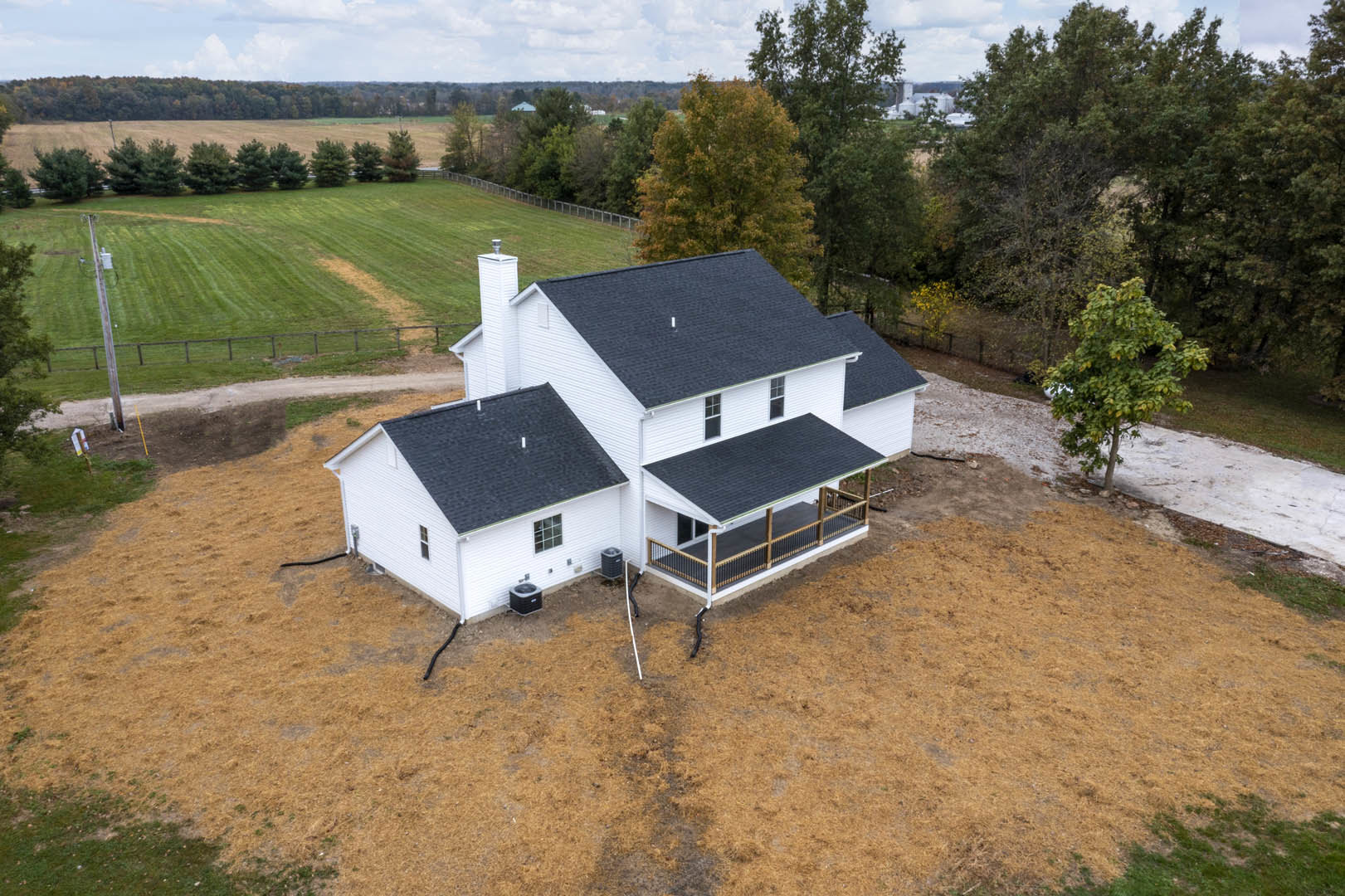 White house with black roof, covered front porch, wooden fence, green grass lawn, leafy tree, blue sky with scattered clouds