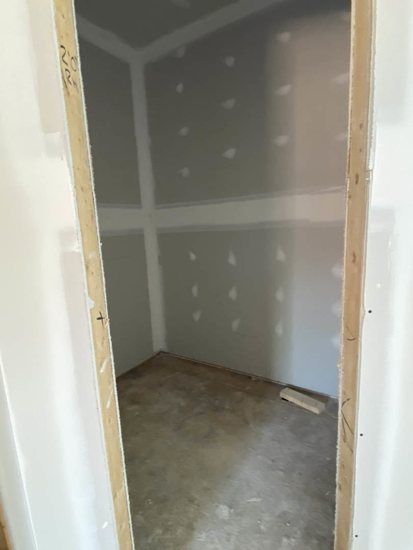Open doorway in a room with concrete flooring, white plaster walls showing small holes, and a piece of wood resting on the floor.