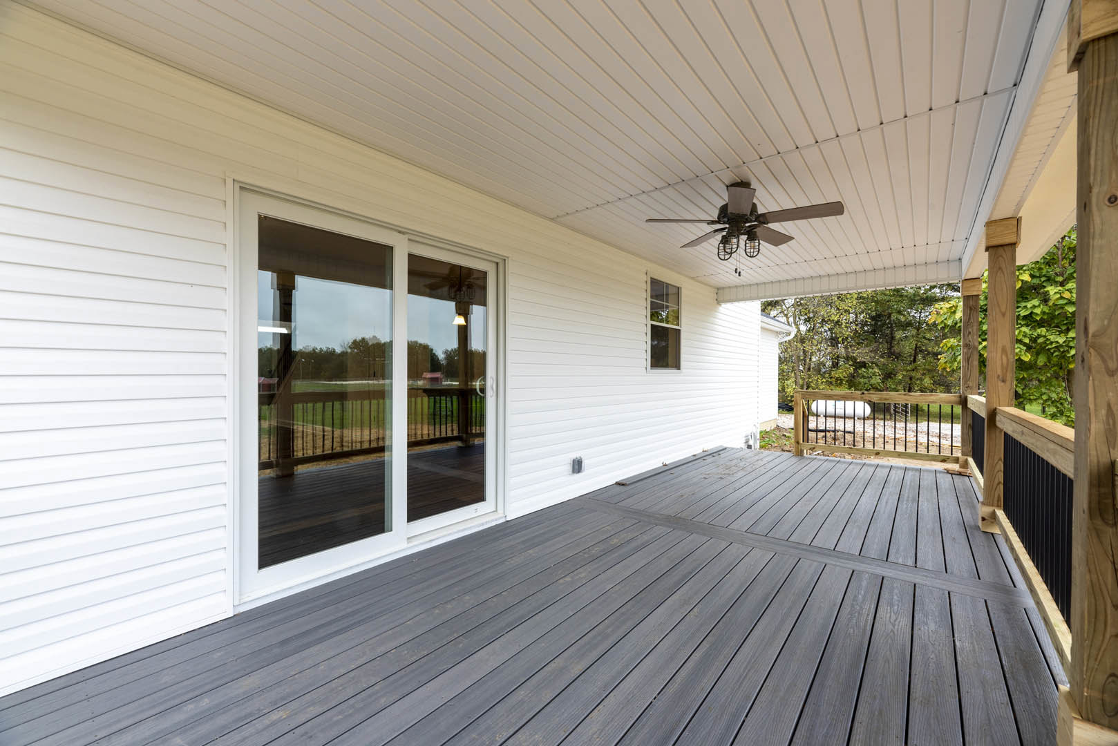 Wood deck with white walls, two ceiling fans with lights, sliding glass door, and white-framed window
