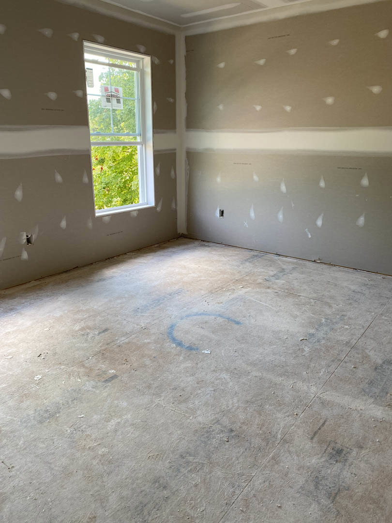 Room with white painted walls, concrete floor, window displaying a sign, and water droplets visible on one wall