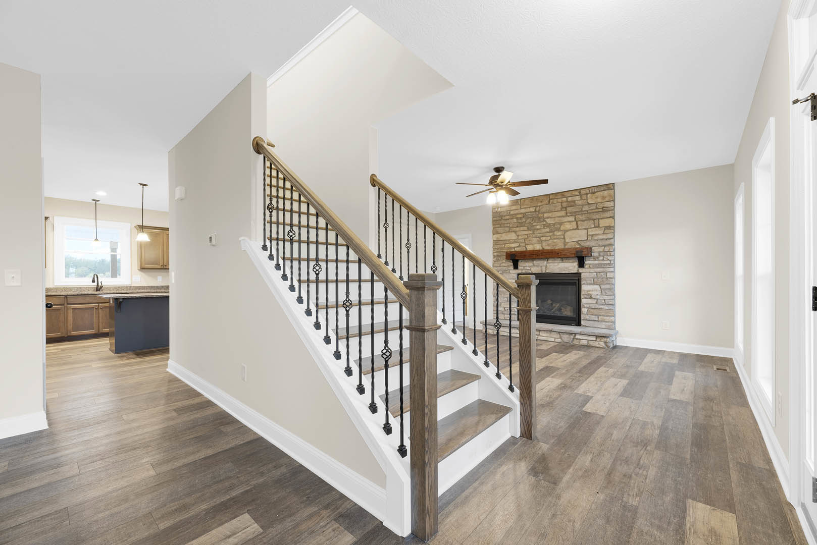 Wood staircase with matching railings and floors, spiral-twist wooden post, ceiling fan with lights, glass-door fireplace, close-up of cabinet, plaster walls, laminate flooring