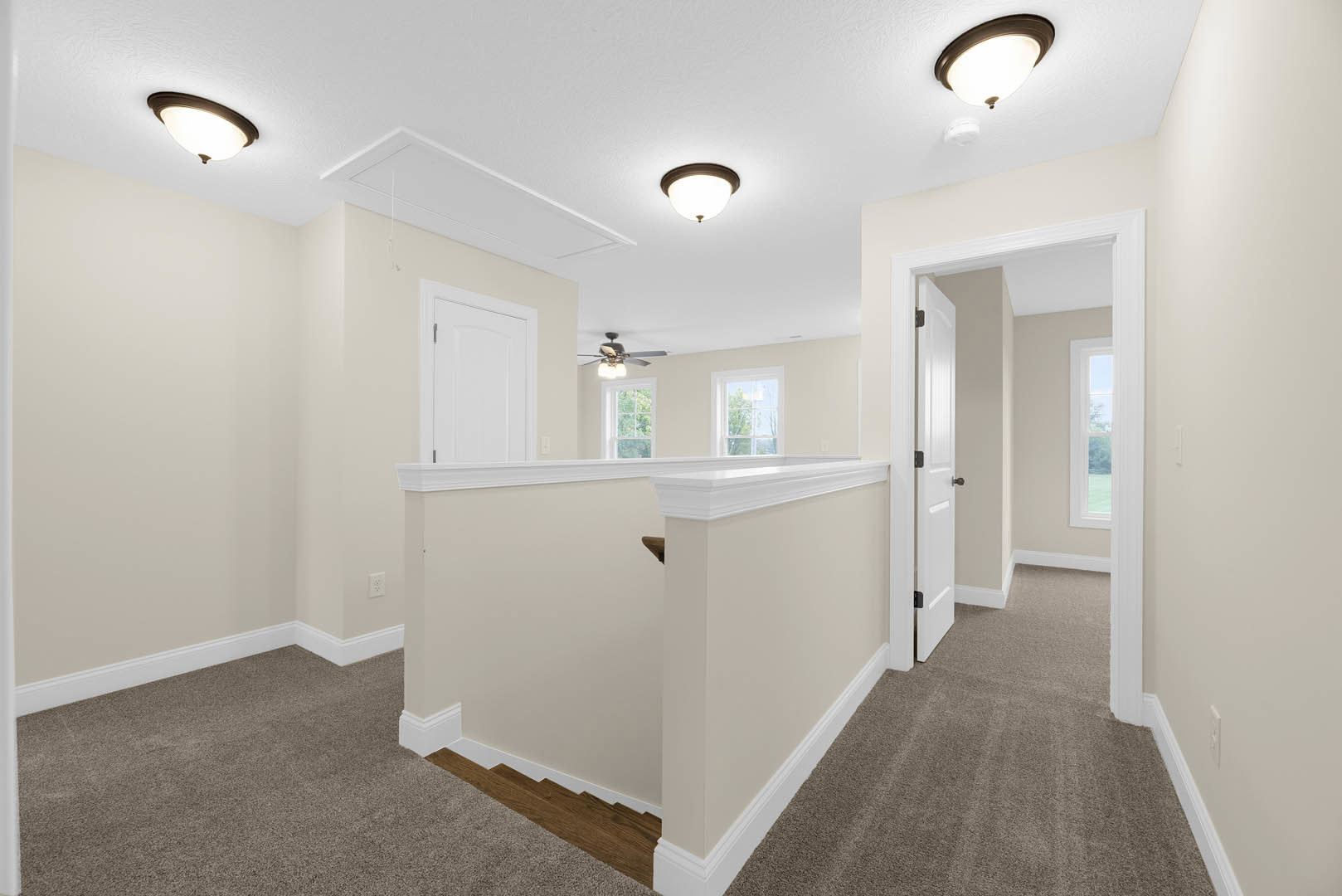 Hallway with laminate flooring, white walls, decorative molding, staircase with wooden steps and white railing, ceiling fan with light fixture, white door with metal handle