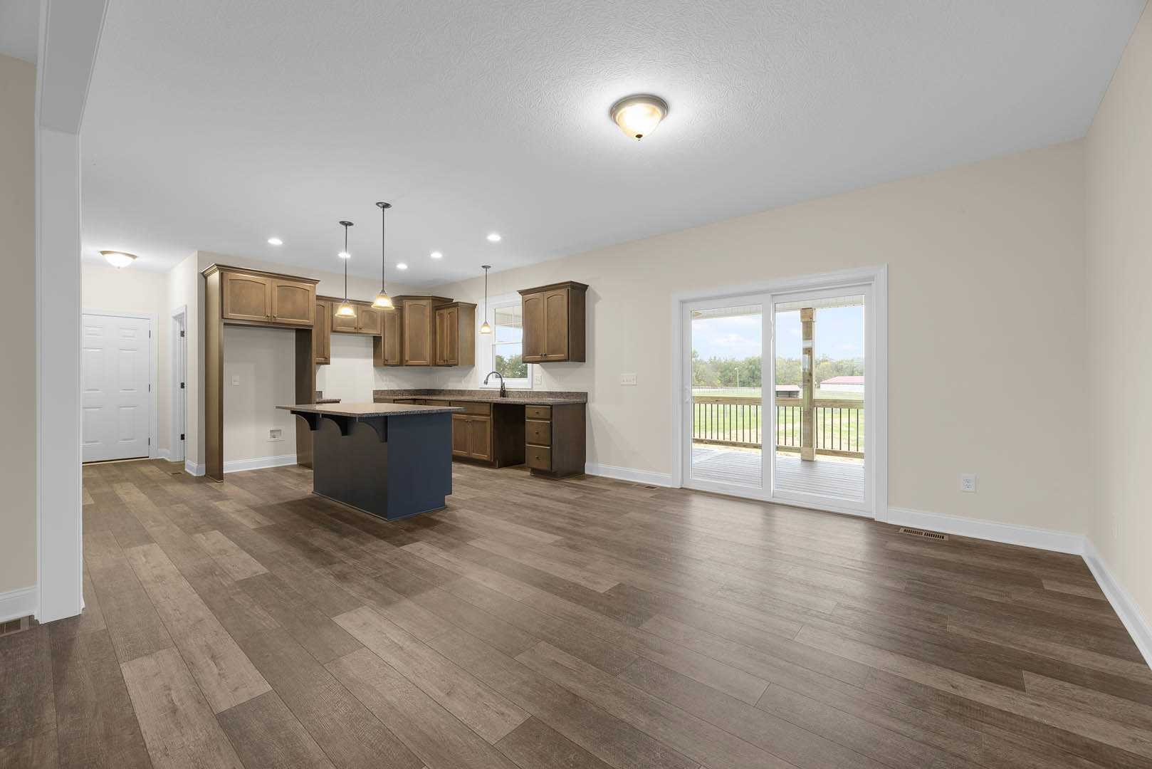 Open-concept kitchen and living room featuring hardwood floors, black cabinetry with marble countertops, sliding glass door leading to a deck overlooking a grassy field, white