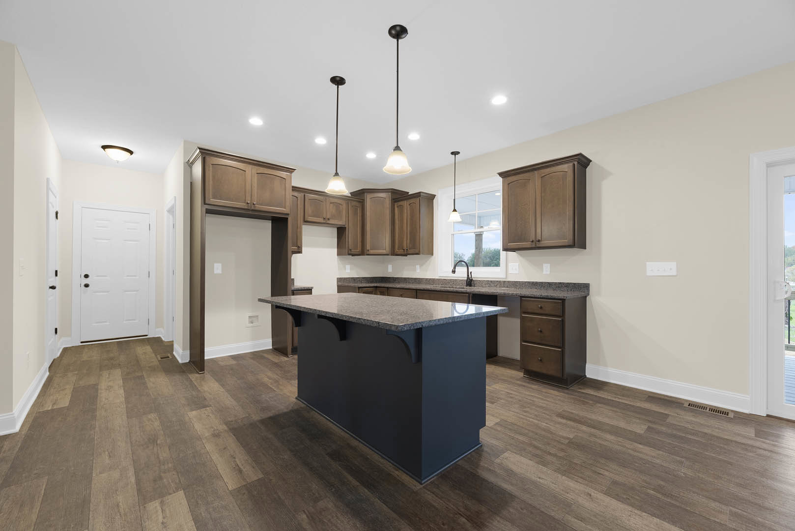 Kitchen with central island featuring granite countertops, wood flooring, white cabinetry with black hardware, pendant light fixture, and white door with black knobs