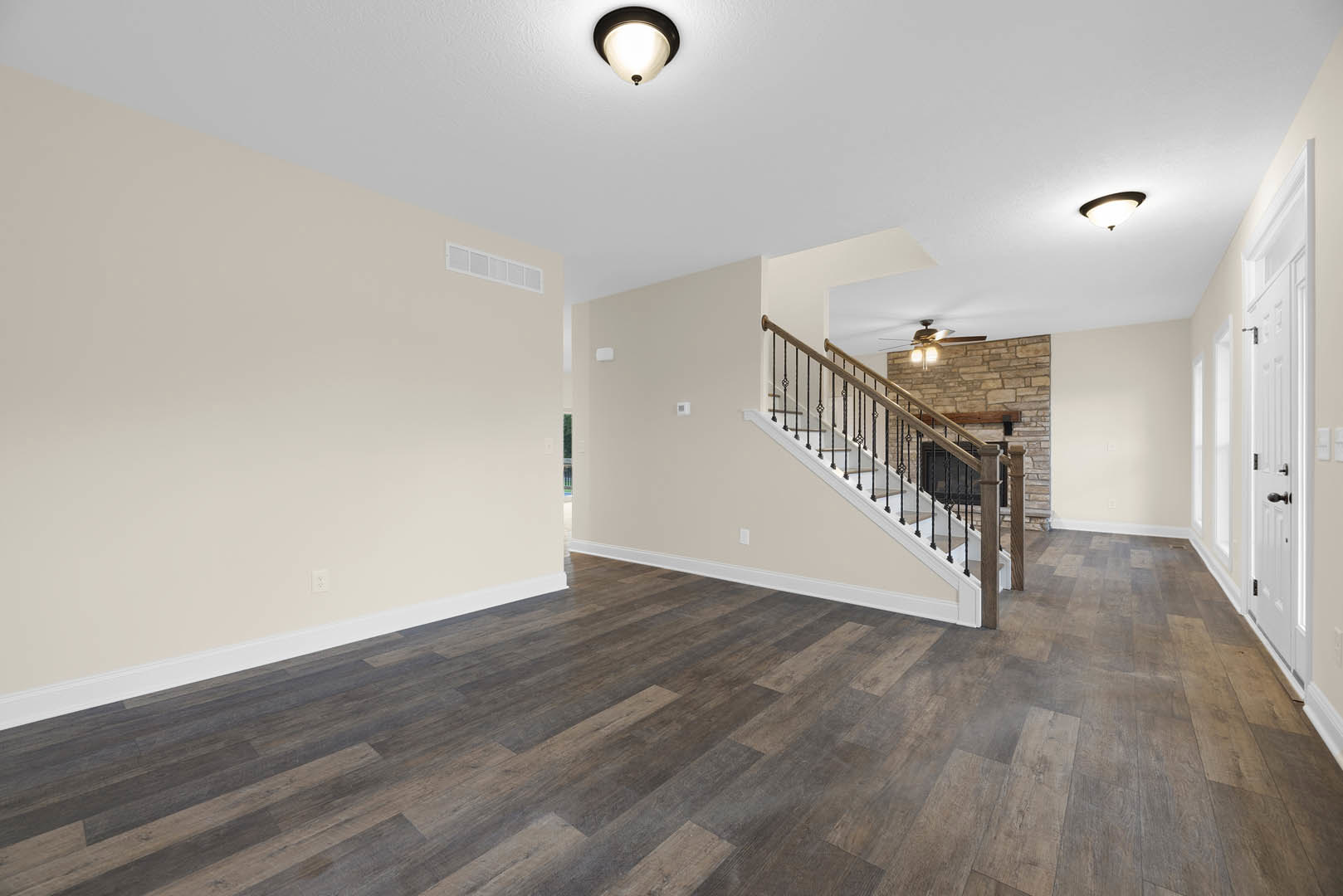 Open living area featuring a wood staircase, exposed brick fireplace, hardwood floors, white plaster walls, and ceiling fan with light fixture.