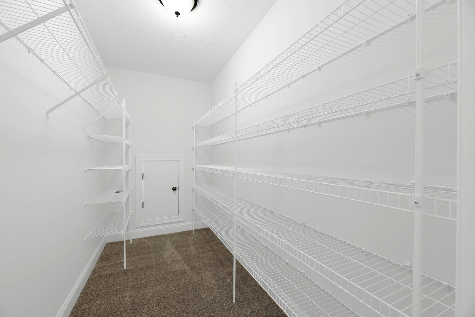 White built-in shelves along a plaster wall, white door with black knob, light fixture on ceiling, beige carpet flooring