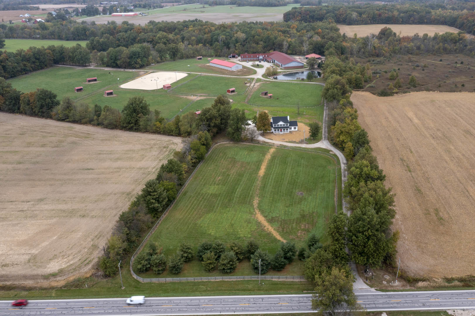 Aerial view of a rural home surrounded by a large grassy field, scattered trees, and a winding path