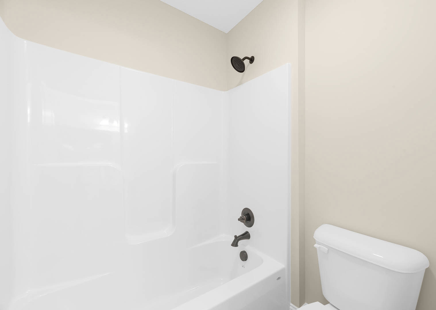 White bathtub and toilet with chrome fixtures in a tiled bathroom, black faucet mounted on a white countertop, shower head with extended arm above tiled wall.