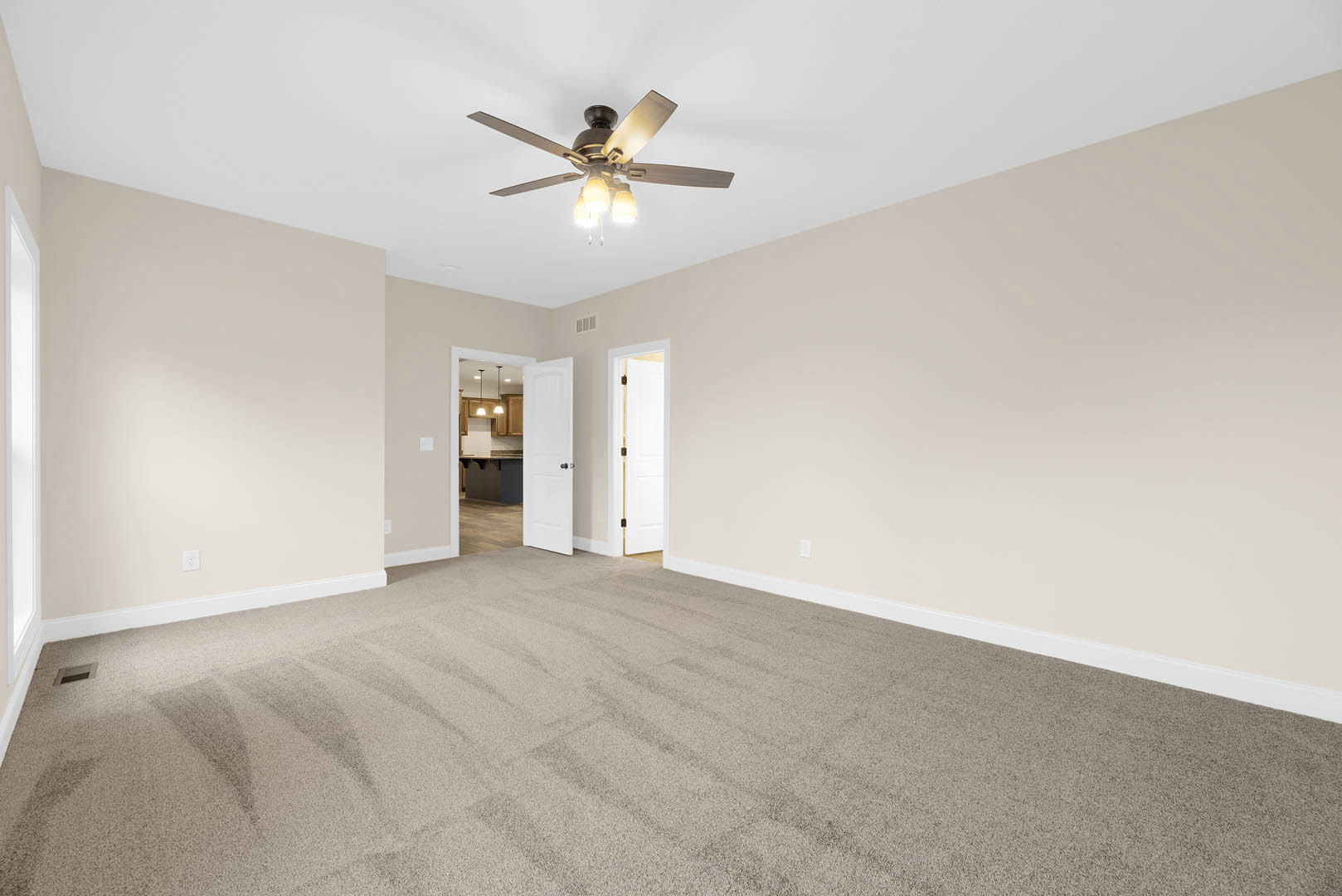 Carpeted room with white walls, ceiling fan with lights, open white door featuring gold handle, rectangular window letting in natural light