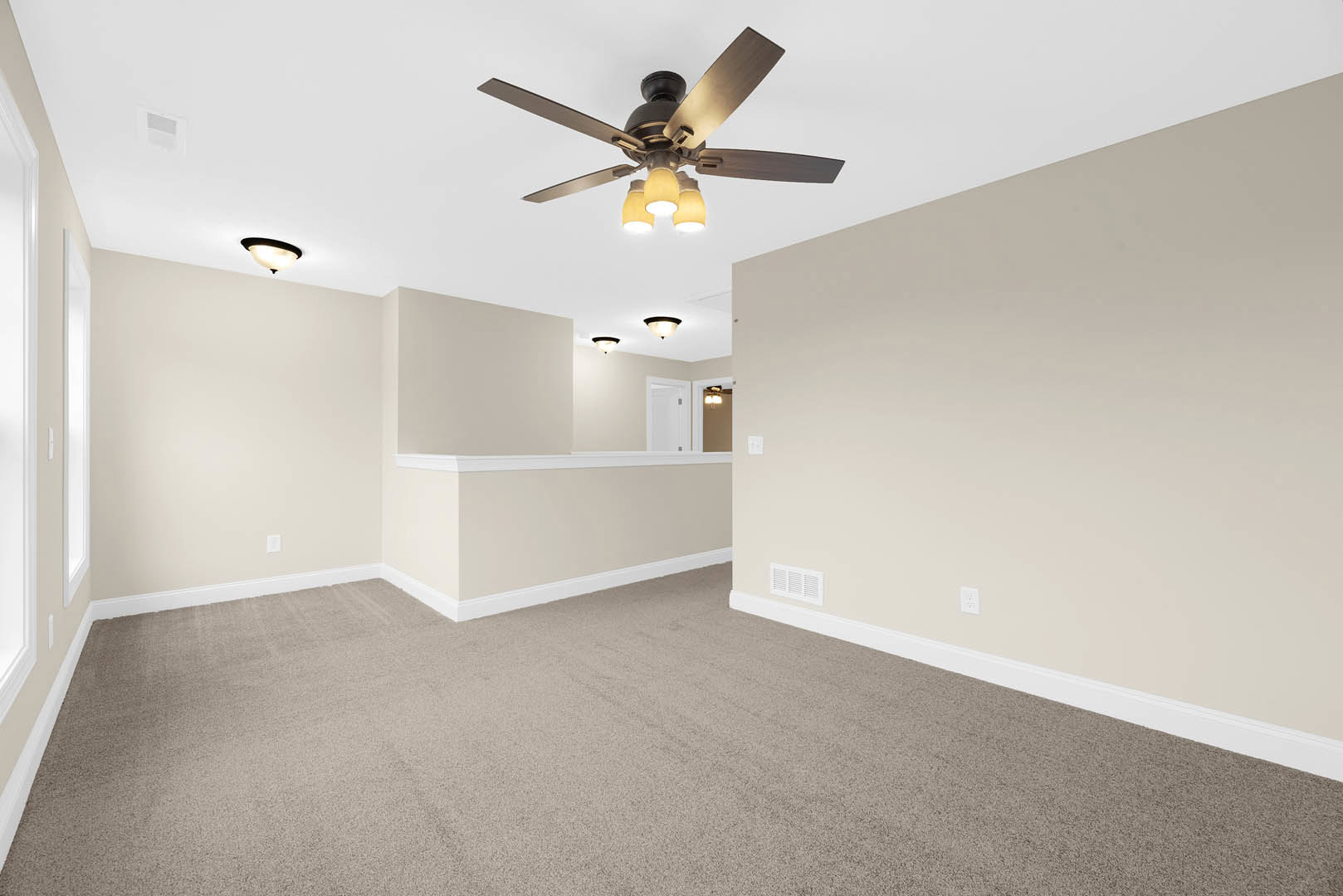 Carpeted living space with white walls, ceiling fan with lights, white door with silver handle, and a built-in counter along one wall
