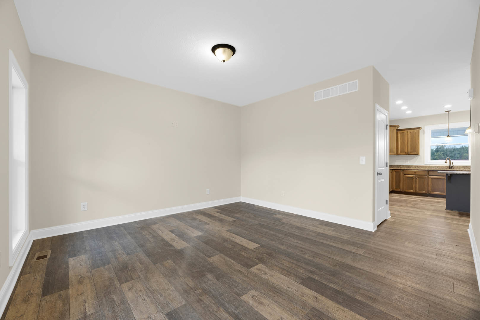 Hardwood floor room featuring a modern light fixture, white door with black handle, white window letting in natural light, and a close-up of a cabinet.